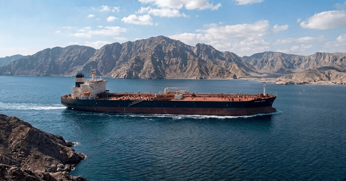 An oil tanker travels through a narrow maritime passage surrounded by rugged coastlines.